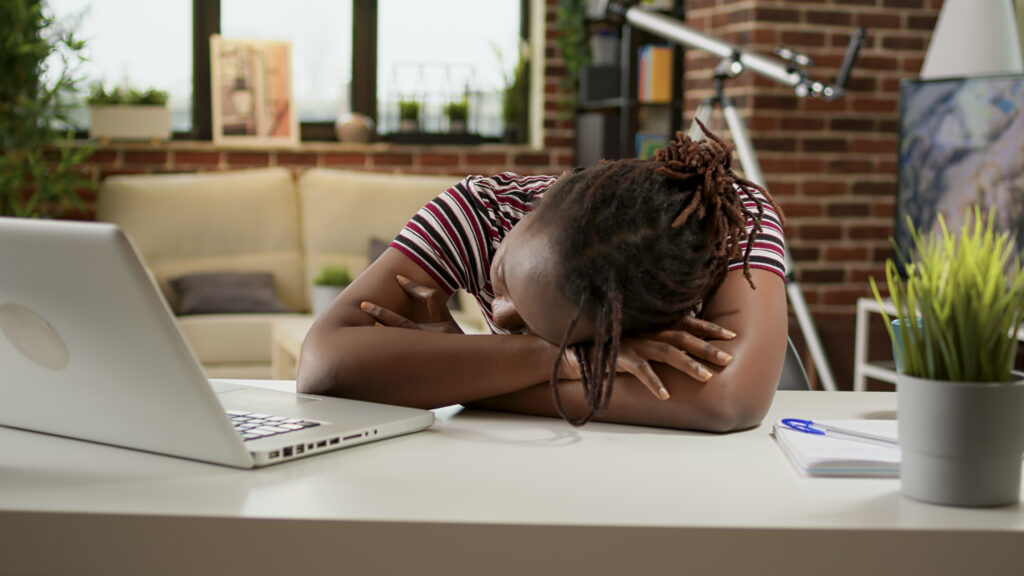 picture of a tired overworked woman falling asleep on a desk with a laptop, working under pressure remotely from home. Procrastination is stealing her time