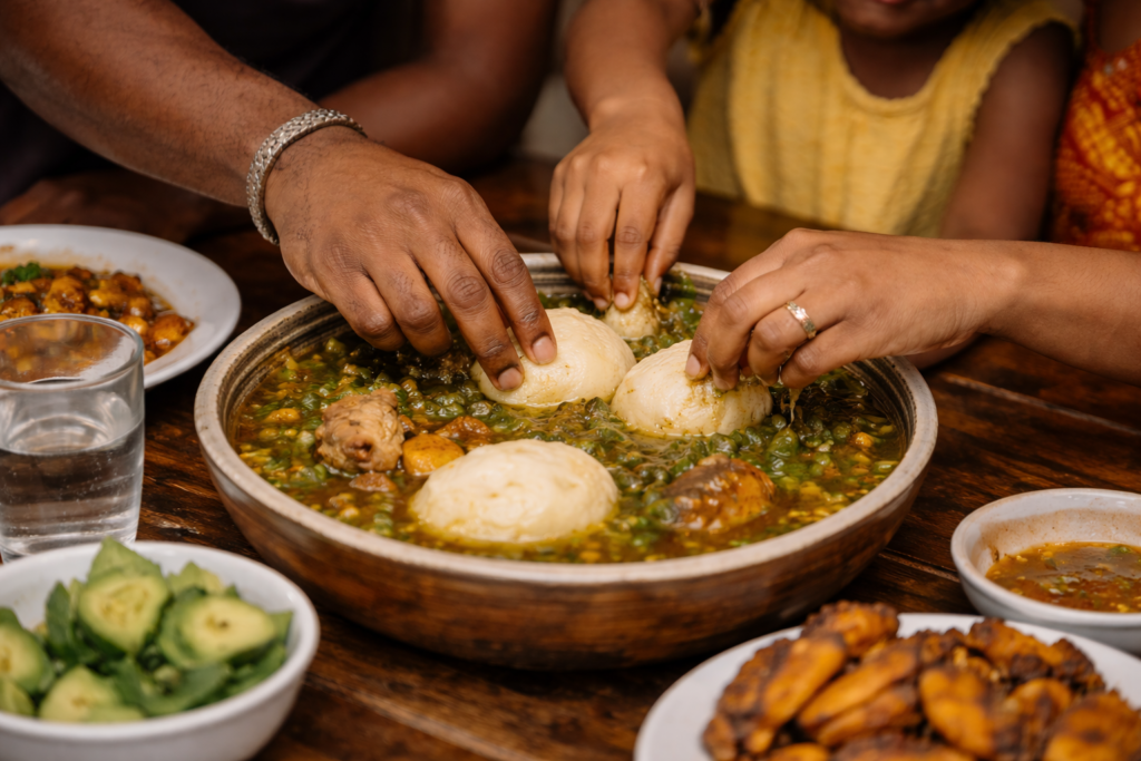 Married Ghanaian couple sharing food from the same plate at a dining table, smiling and talking in soft natural light