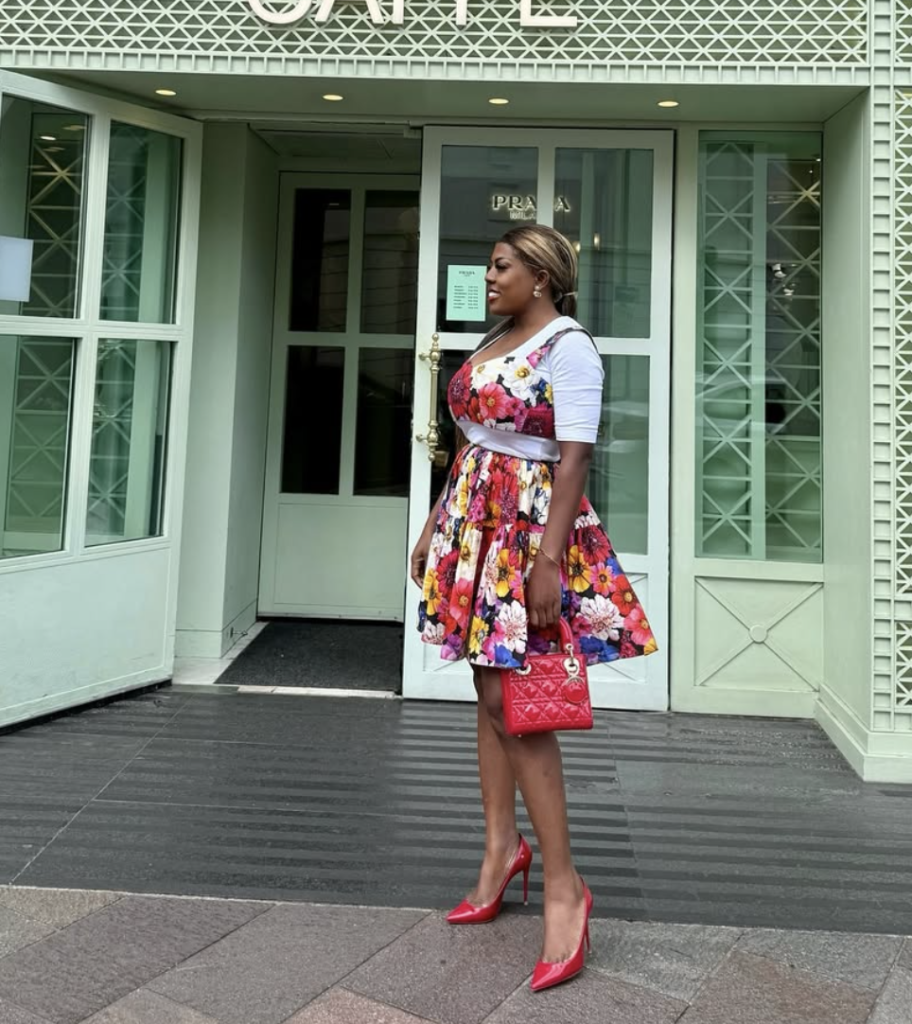 Nana Aba Anamoah wearing a floral dress with red heels and handbag outside a boutique.