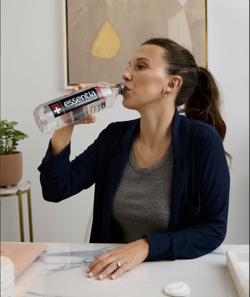 Millie Bobby Brown casually drinking bottled water indoors, natural look, relaxed and focused