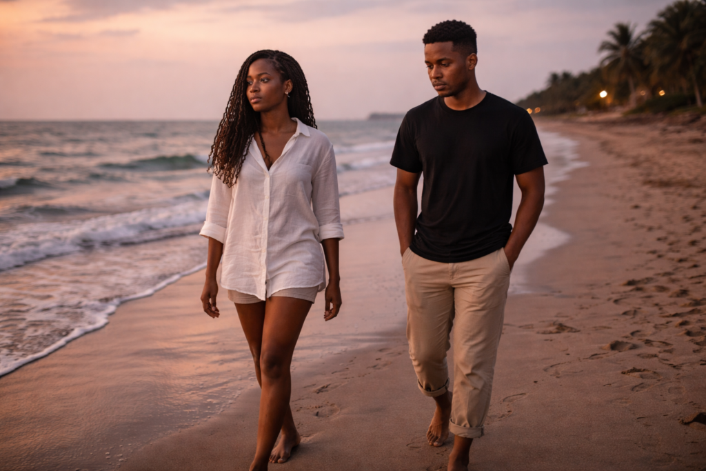 Ghanaian couple walking barefoot on a beach at dusk with emotional distance between them, not touching