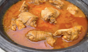 Close-up of Ghanaian light soup with chicken in a light red oily broth showing authentic texture