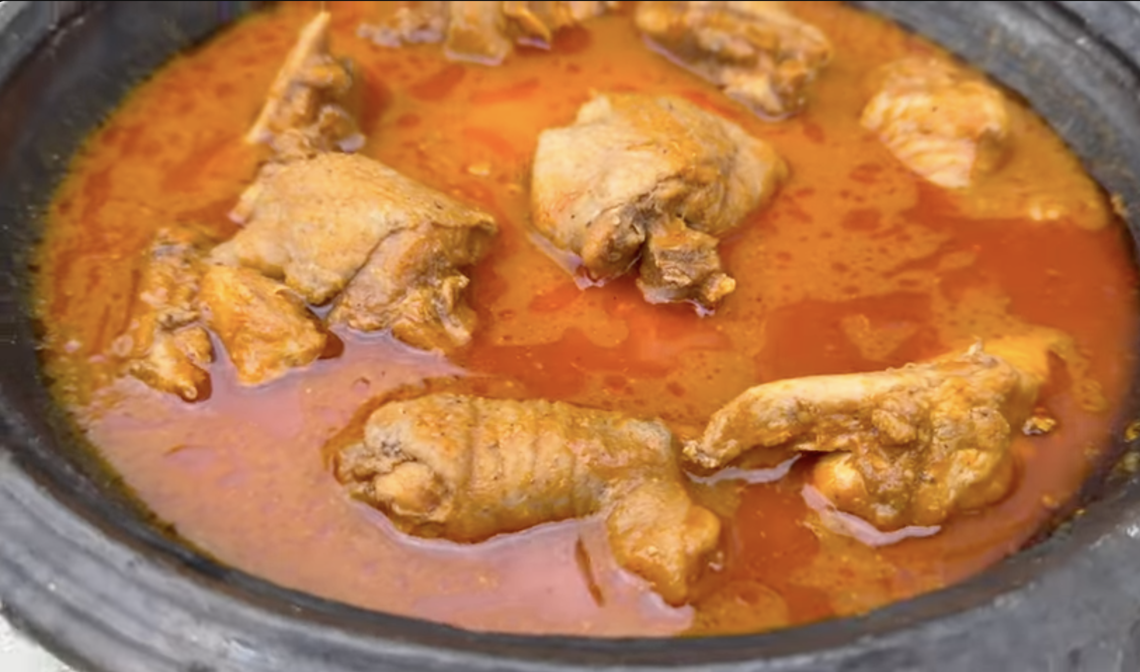 Close-up of Ghanaian light soup with chicken in a light red oily broth showing authentic texture