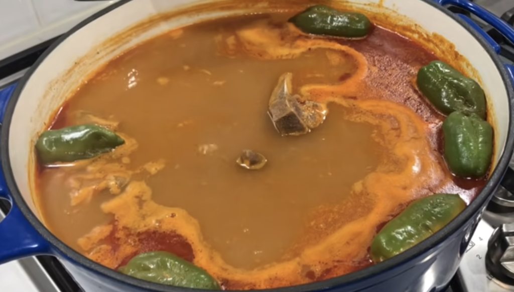 Authentic Ghanaian light soup with goat meat and whole pepper simmering in a pot with light oily broth