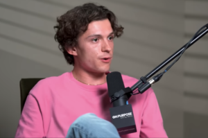 Tom Holland speaking into a microphone during Jay Shetty podcast interview, wearing a pink shirt, discussing social media and mental health