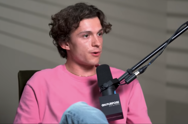 Tom Holland speaking into a microphone during Jay Shetty podcast interview, wearing a pink shirt, discussing social media and mental health