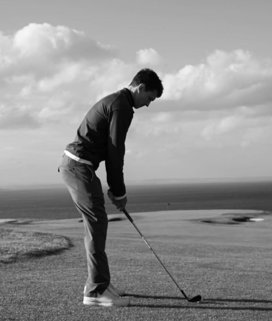 Tom Holland playing golf alone on a scenic course, captured in black and white with ocean view