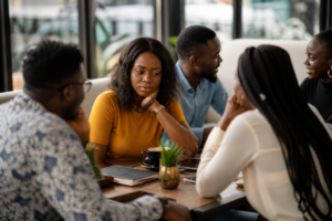 Group of African adults having a casual conversation in a café while one woman sits thoughtfully.