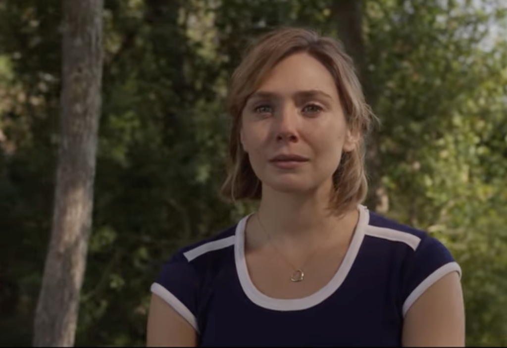 Close-up of a woman outdoors with teary eyes and an emotional expression in a tense moment from Love & Death.