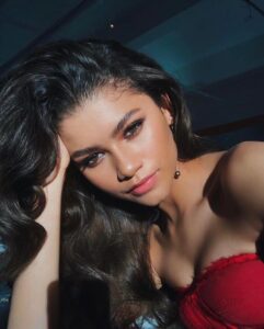 Zendaya in glamorous makeup and a red outfit posing confidently for a selfie.