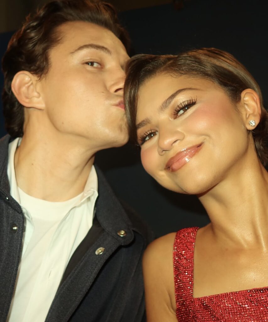 Tom Holland kisses Zendaya on the head as the couple pose for a selfie together.