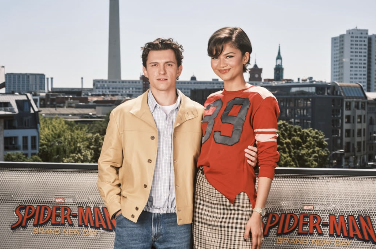 Tom Holland and Zendaya pose together during the Spider-Man: Brand New Day press tour, smiling for photographers.