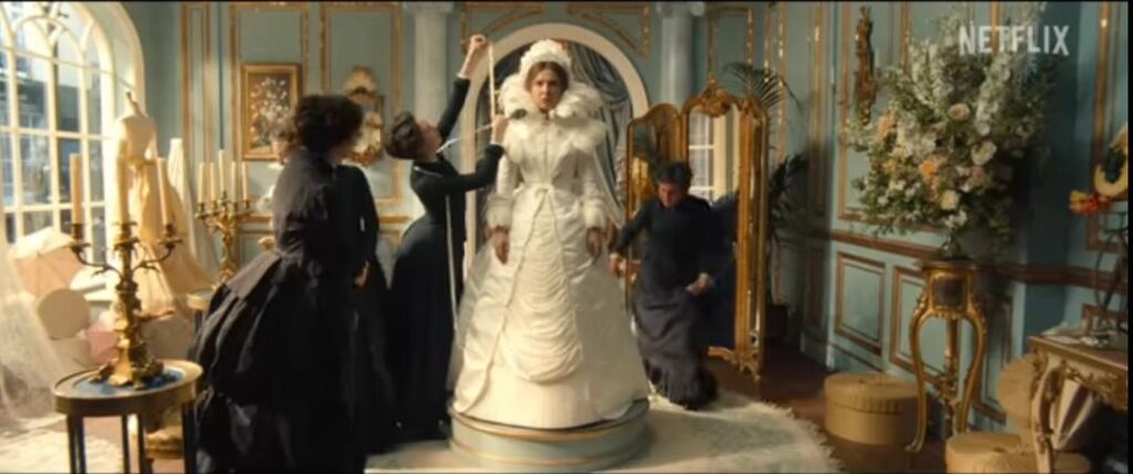 Enola Holmes stands while attendants prepare her elaborate wedding gown in Enola Holmes 3.