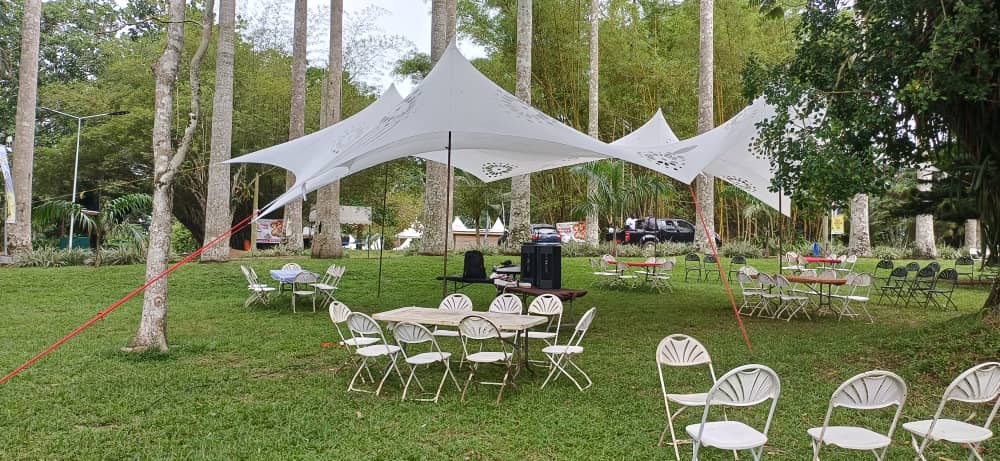 Landscaped outdoor event space with green grass, trees, tables, chairs and white canopy tents.